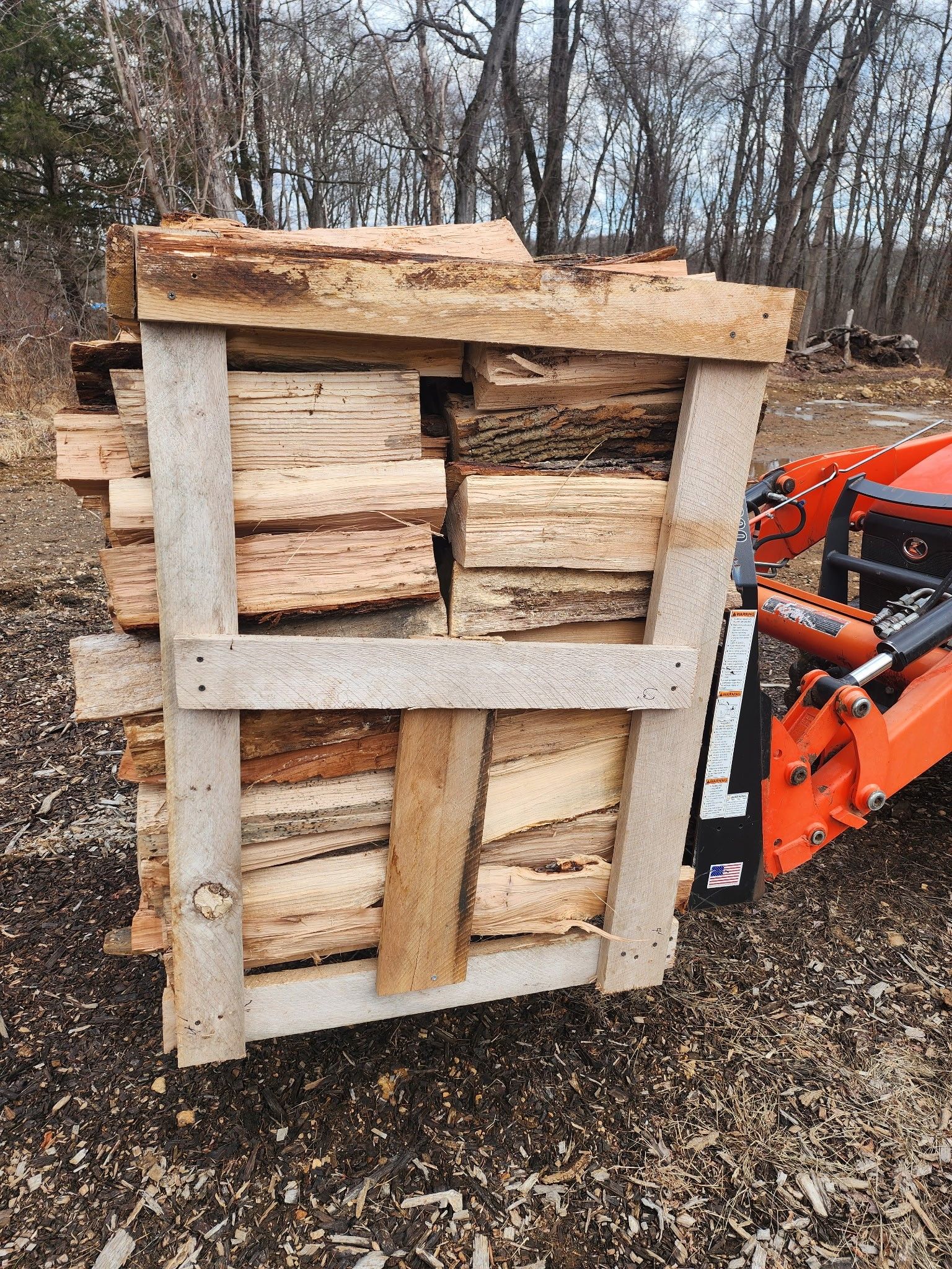 A pile of wood is sitting on top of a wooden pallet next to a tractor.