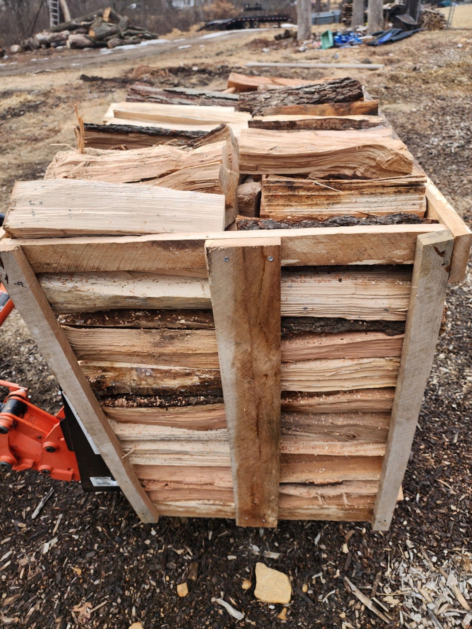 A wooden crate filled with logs is sitting on the ground.