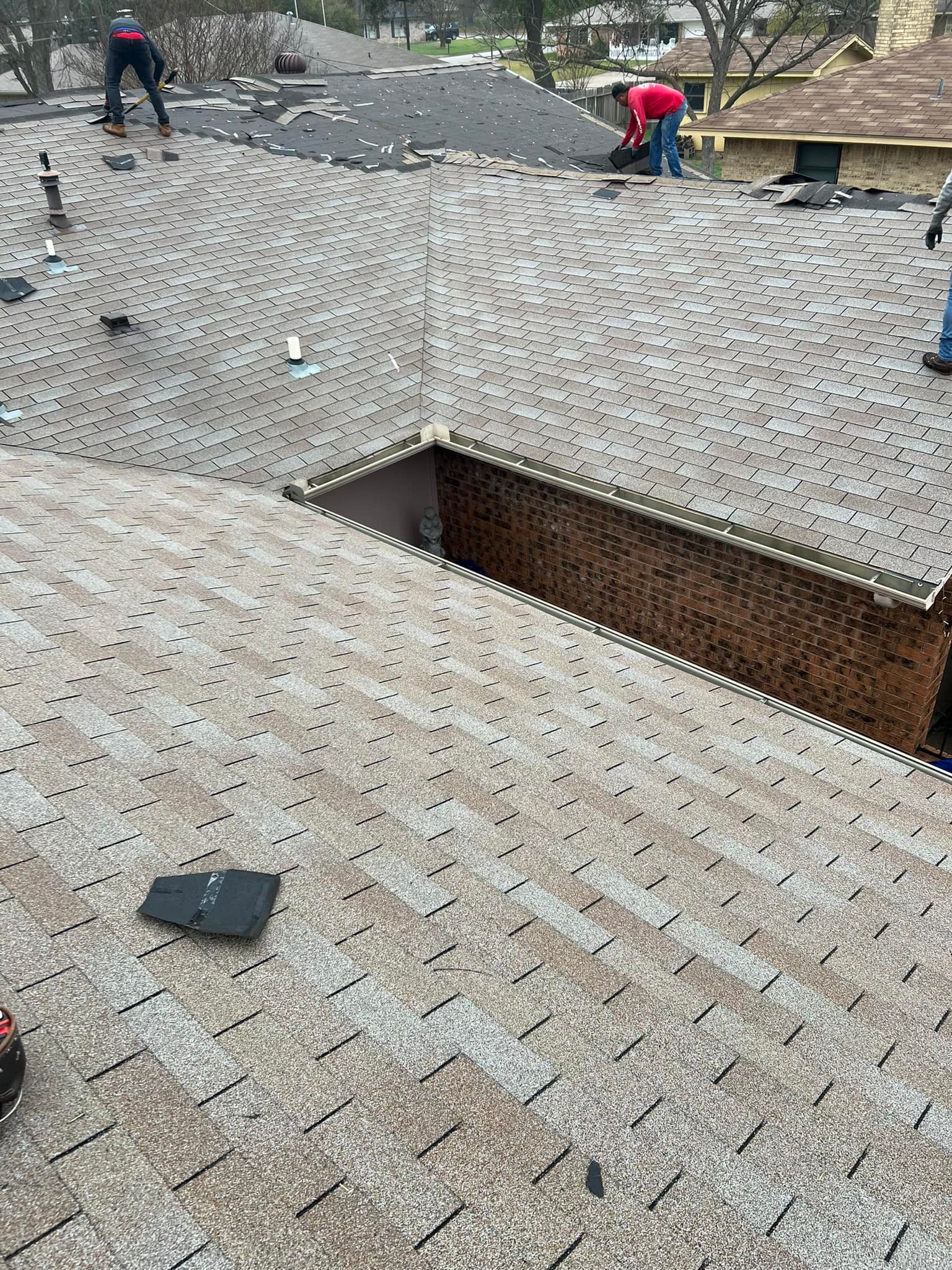 Workers repairing a shingled roof with a large open section in the middle