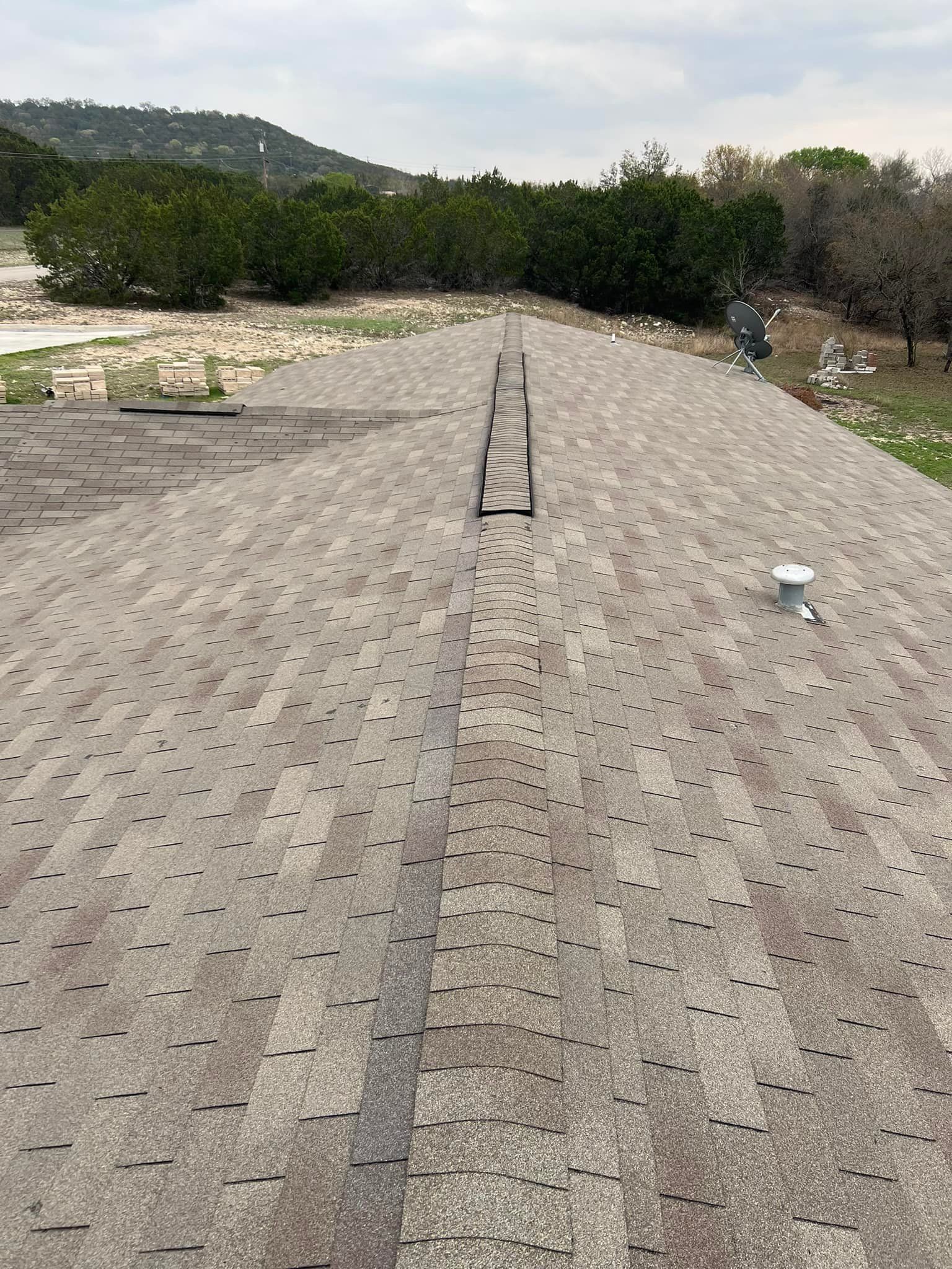 Rooftop walkway with gray pavers, central drainage strip, and trees and hills in the background