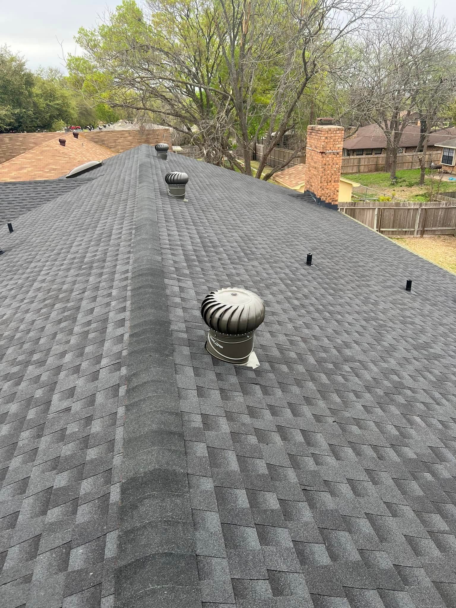 Shingled roof with two turbine vents and a chimney, viewed from above in a suburban neighborhood