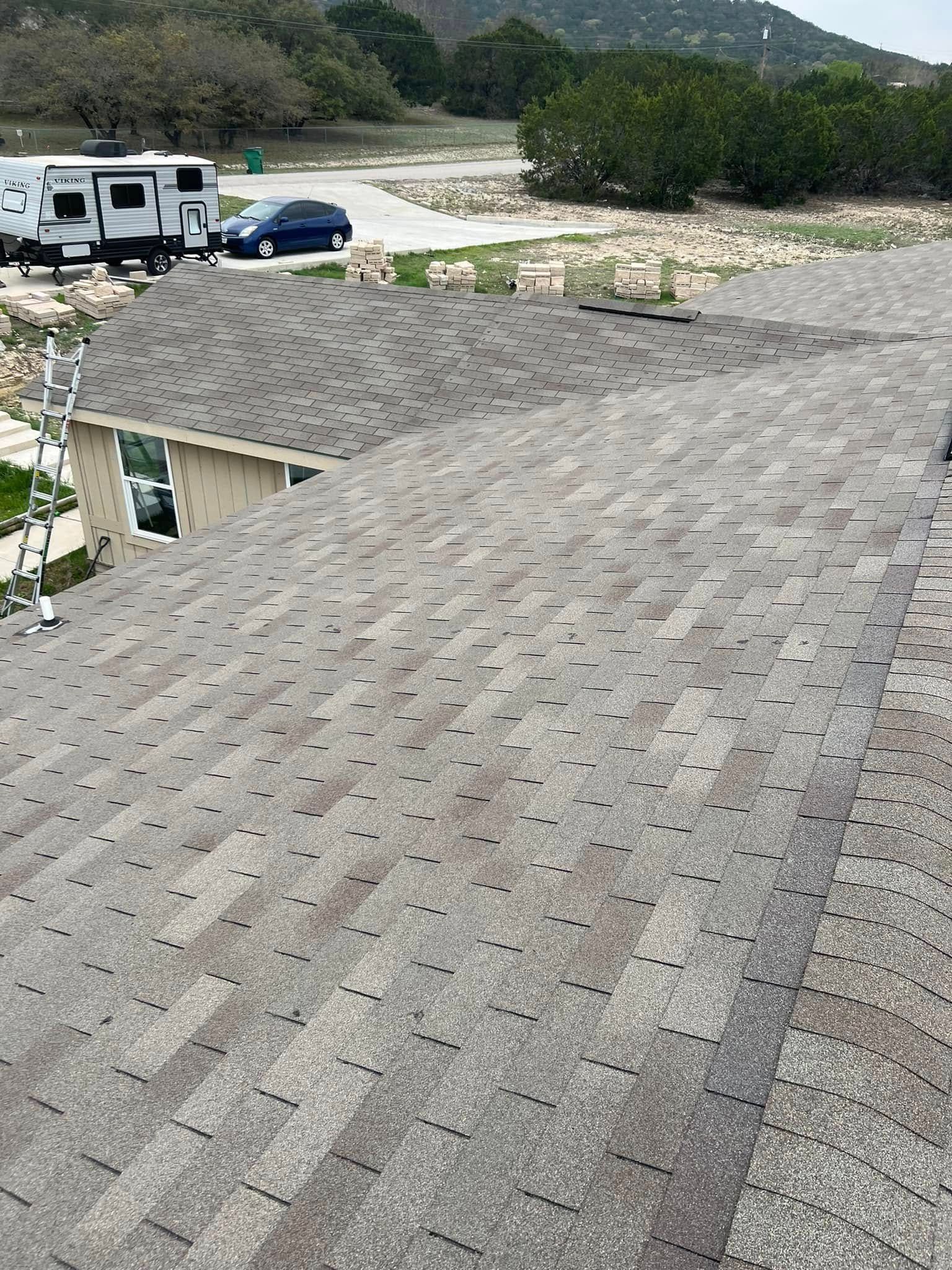 Rooftop with gray shingles overlooking parked vehicles and a wooded hillside under cloudy skies