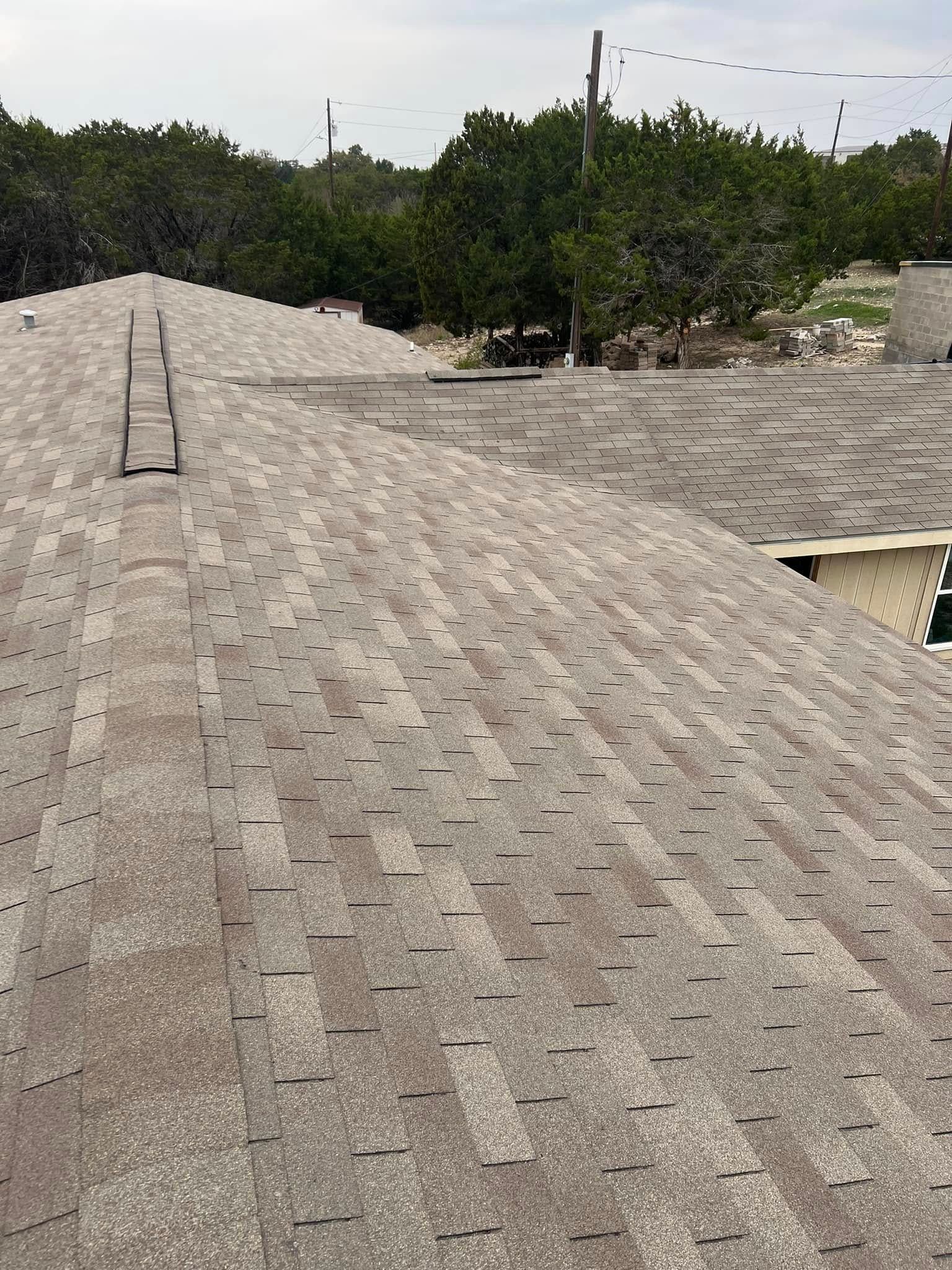 Roof shingles on a house with trees and utility lines in the background.
