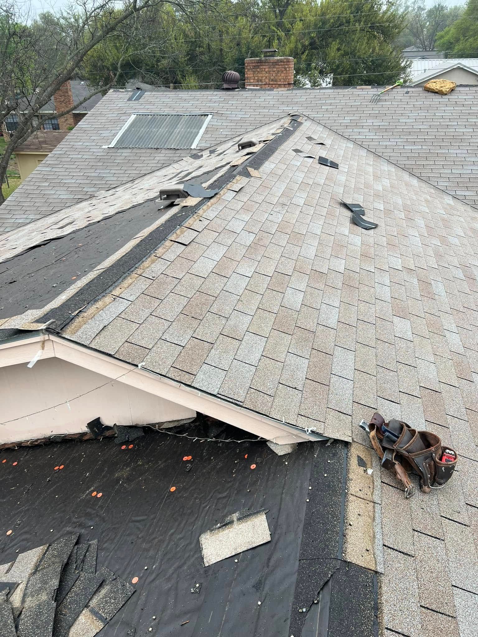 Collapsed roof with torn shingles and exposed underlayment on a house after storm damage
