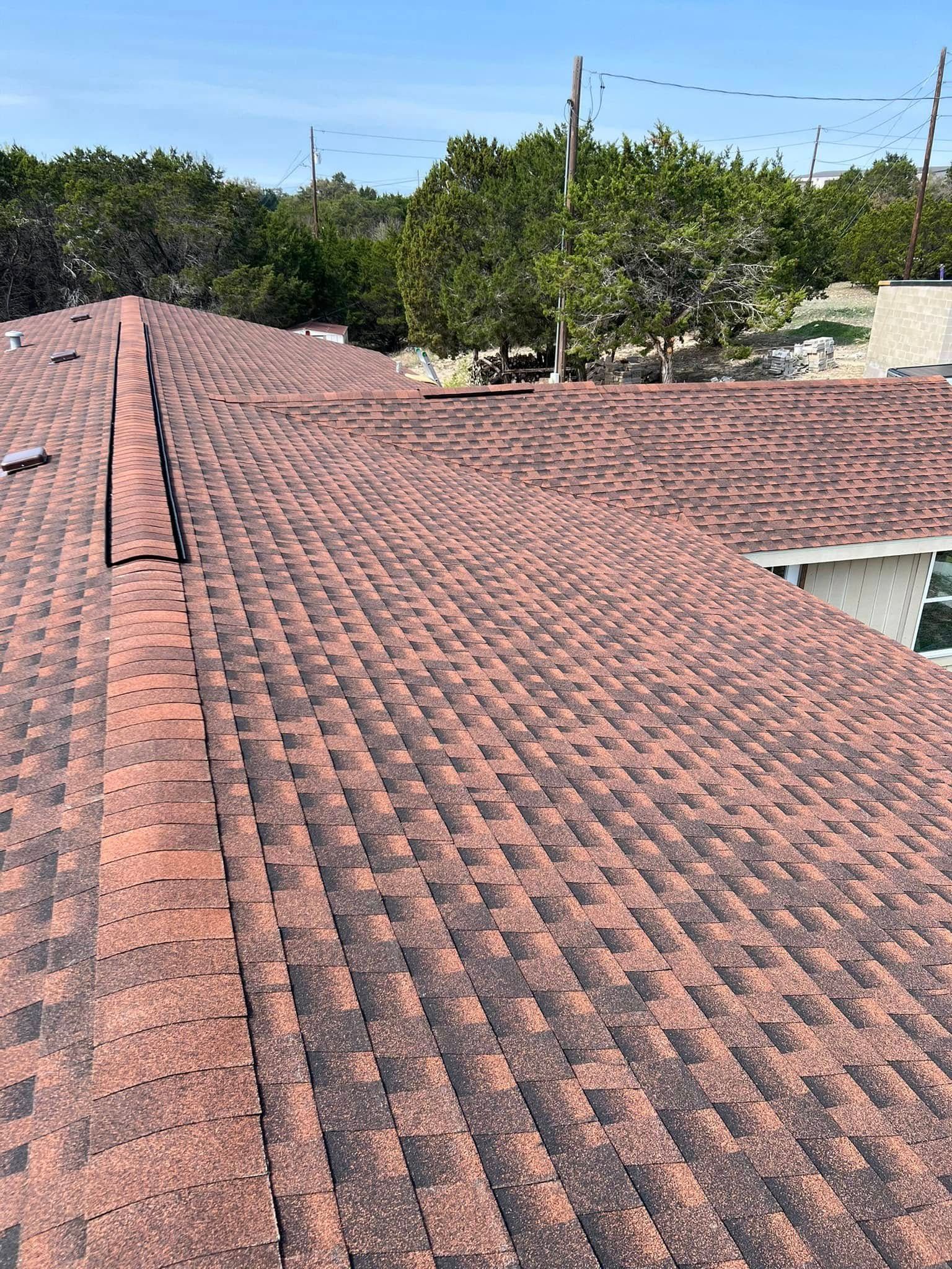 Red shingle rooftop with trees and houses in the background under a clear sky