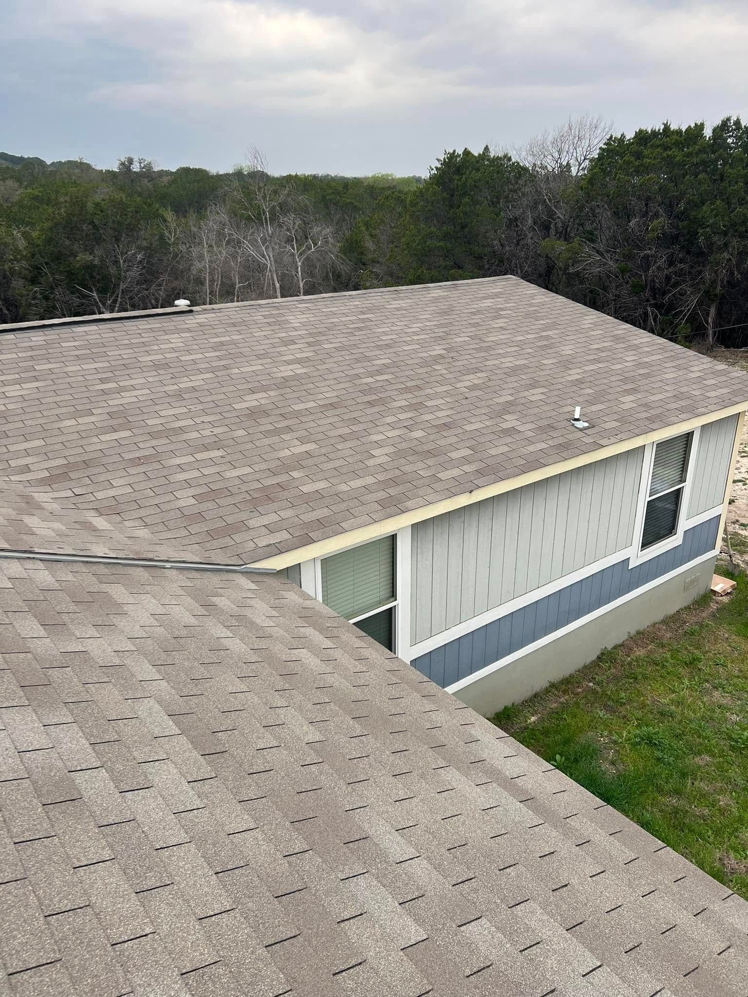 Aerial view of a gray-shingled house roof with trees and grass around it.
