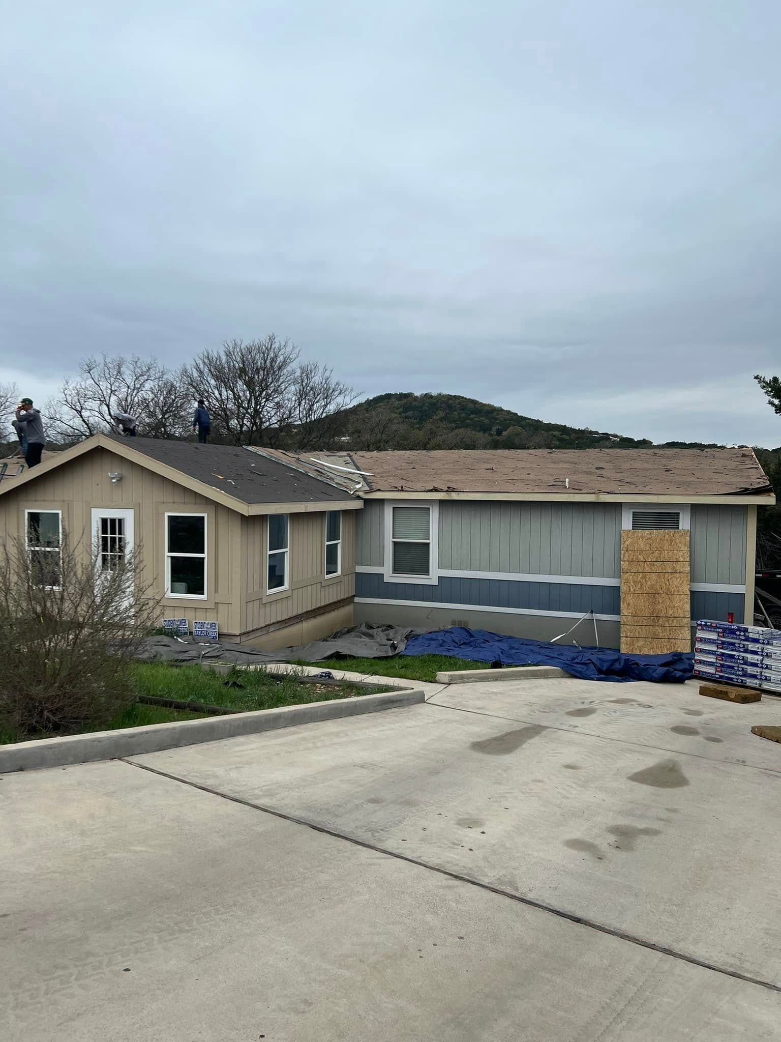 Single-story house with a concrete driveway, blue tarp, and cloudy sky