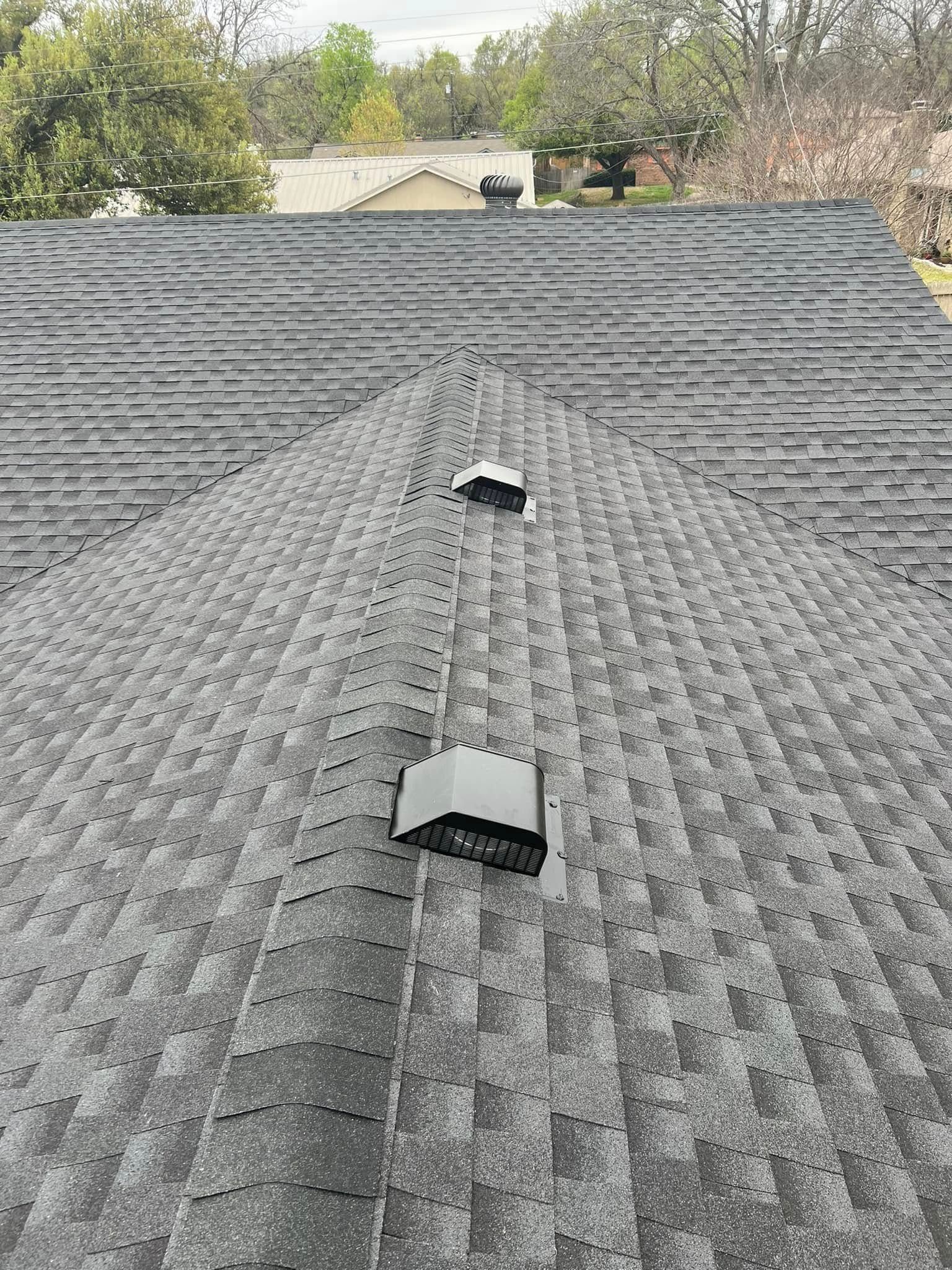 Roof with gray asphalt shingles and two vents, viewed from above with trees in the background