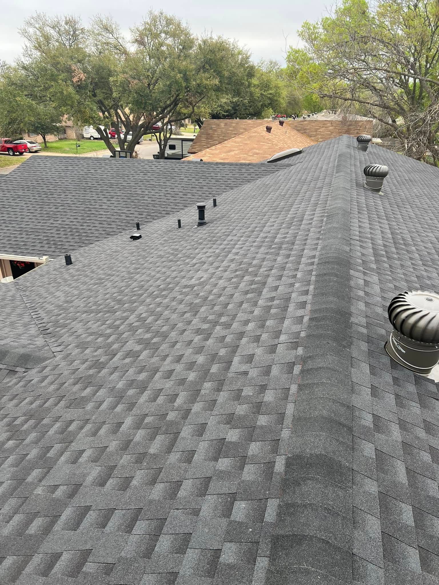 New asphalt shingle roof with vents, viewed from the ridge in a residential neighborhood