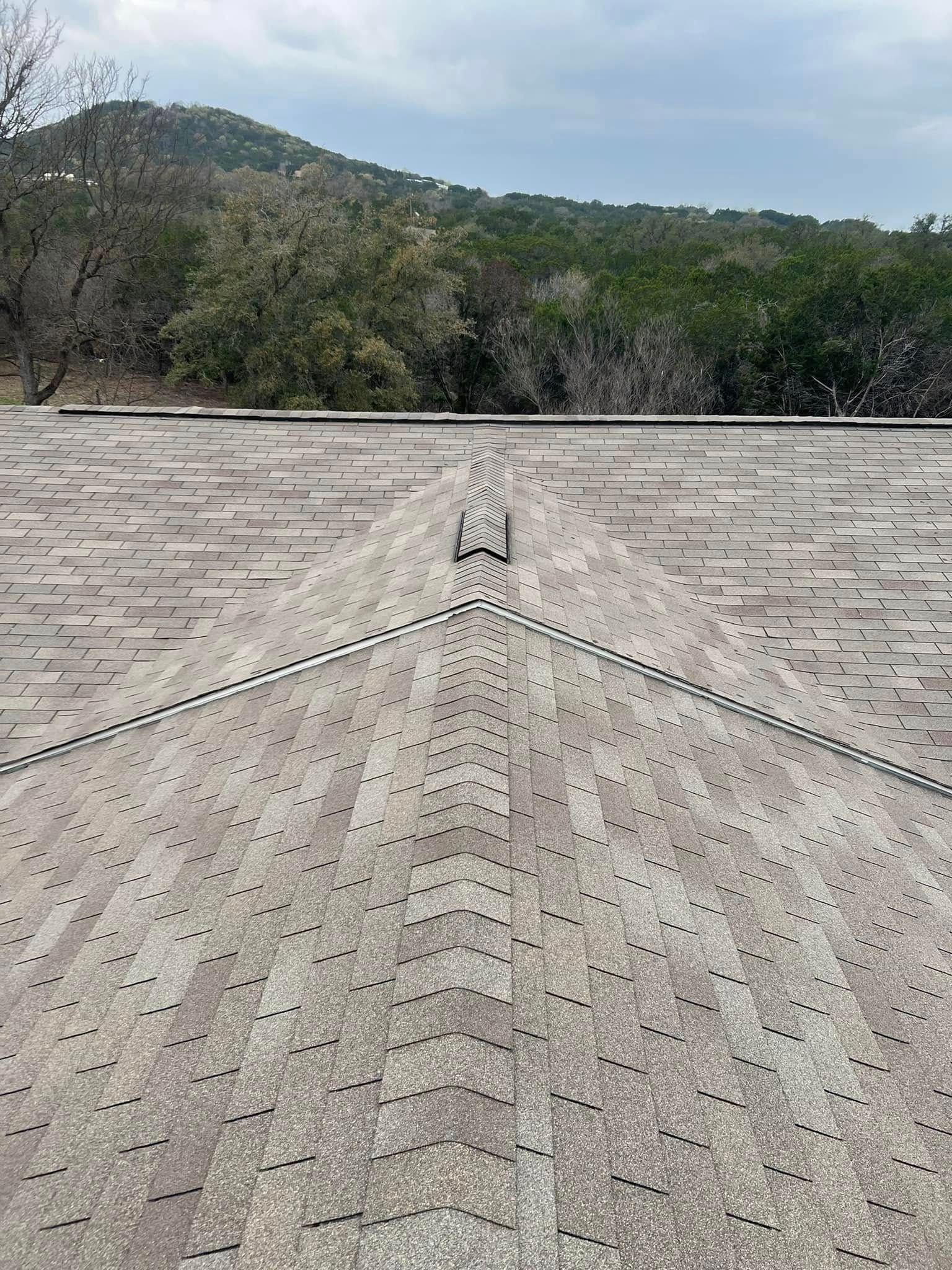 Roof shingles leading to a valley peak, with trees and hills in the background