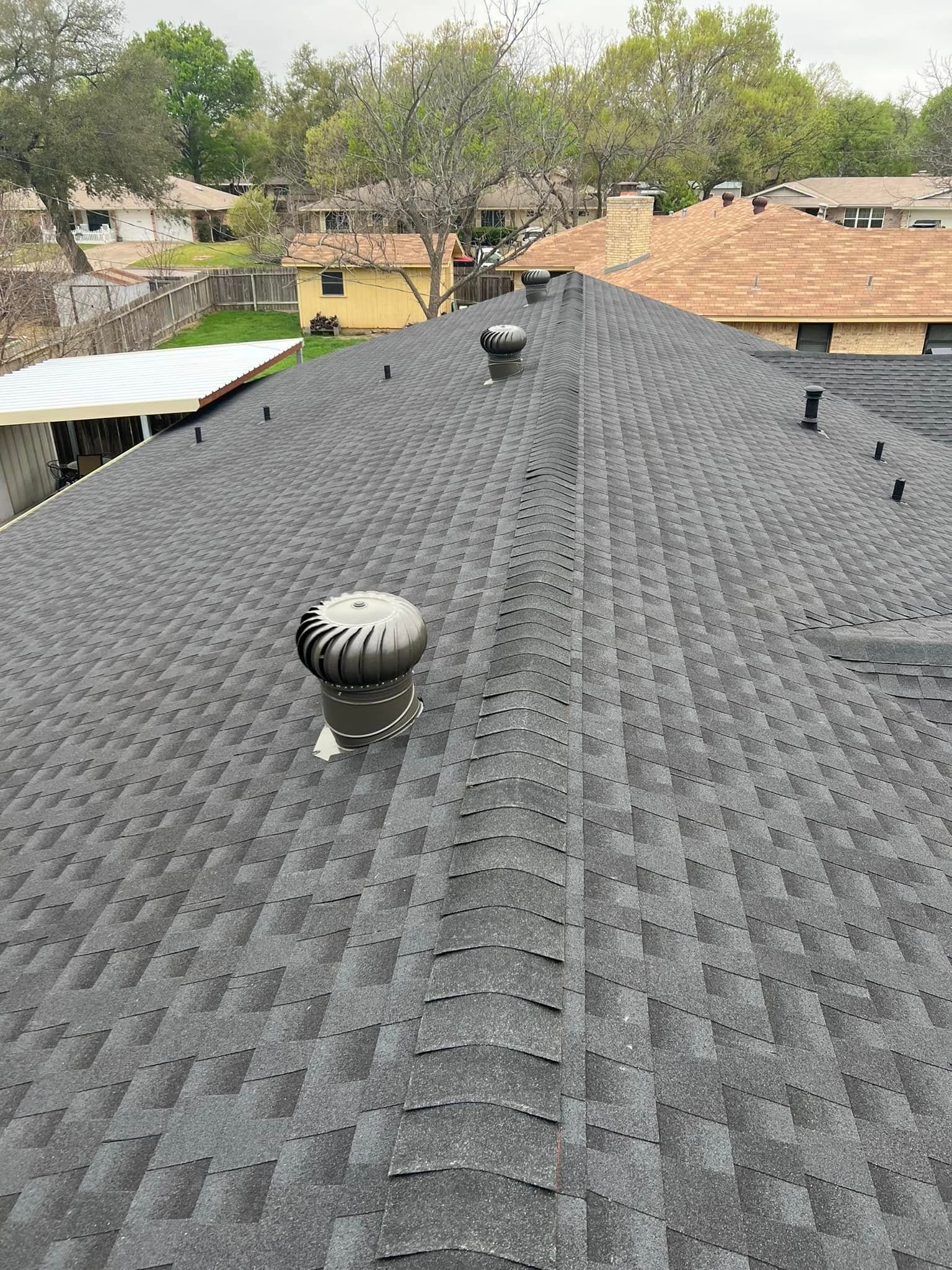 Rooftop with gray shingle roofing and three black vent caps, viewed from above across a neighborhood