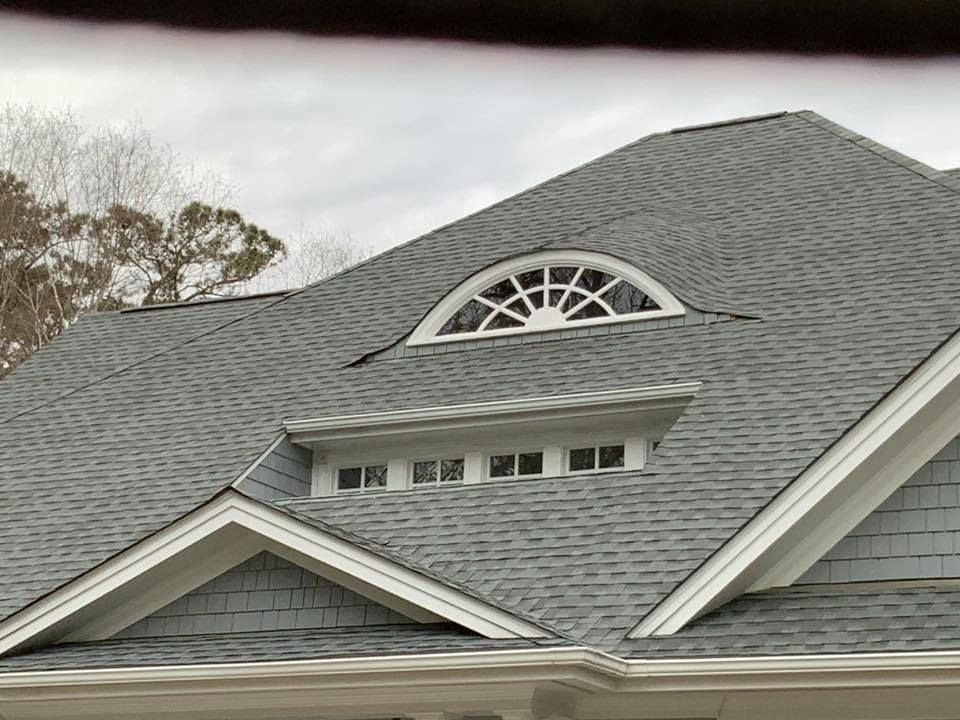 Gray shingled roof with a small arched dormer window under an overcast sky