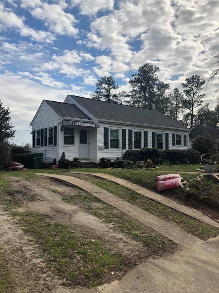 Small white house with a front porch on a sloped dirt driveway under a cloudy sky.
