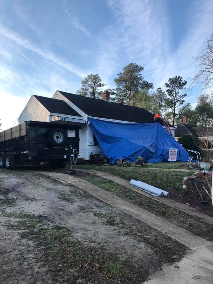 House under repair with blue tarp covering the side and a trailer parked beside it