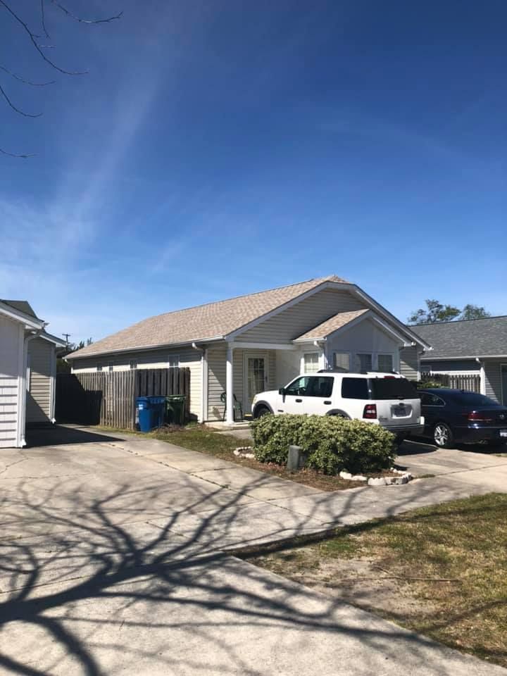 Suburban house with two parked SUVs, driveway, and bare tree shadows under a clear blue sky