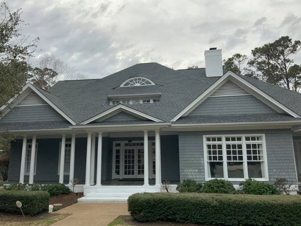 Gray house with white columns, front porch, and landscaped shrubs under a cloudy sky