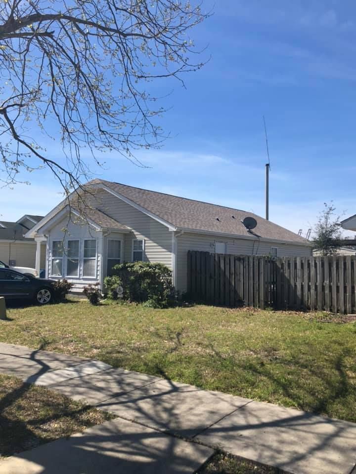 Suburban house with gray siding, fenced yard, and sidewalk under a clear blue sky