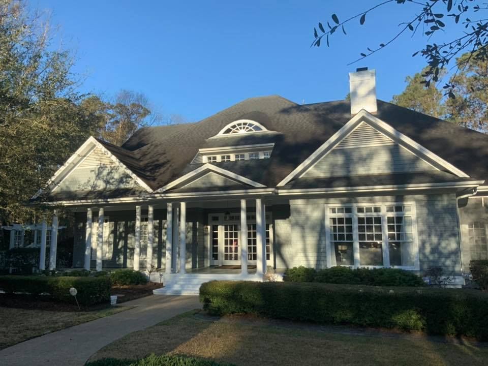 Suburban stone house with a front porch, gabled roof, and manicured hedges in sunlight