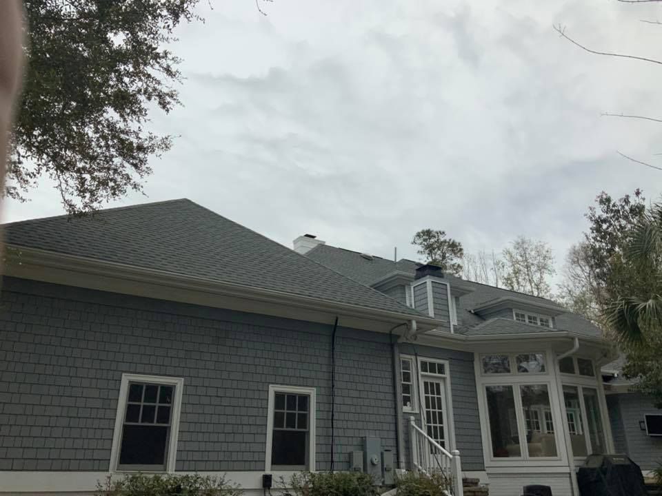 Gray house exterior with shingled roof, white trim, and covered porch under a cloudy sky