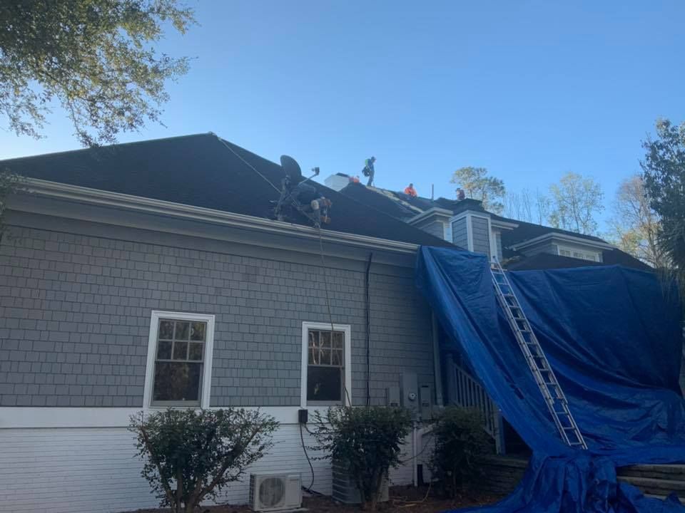 Gray house with blue tarp covering roof damage and ladders leaning against the side
