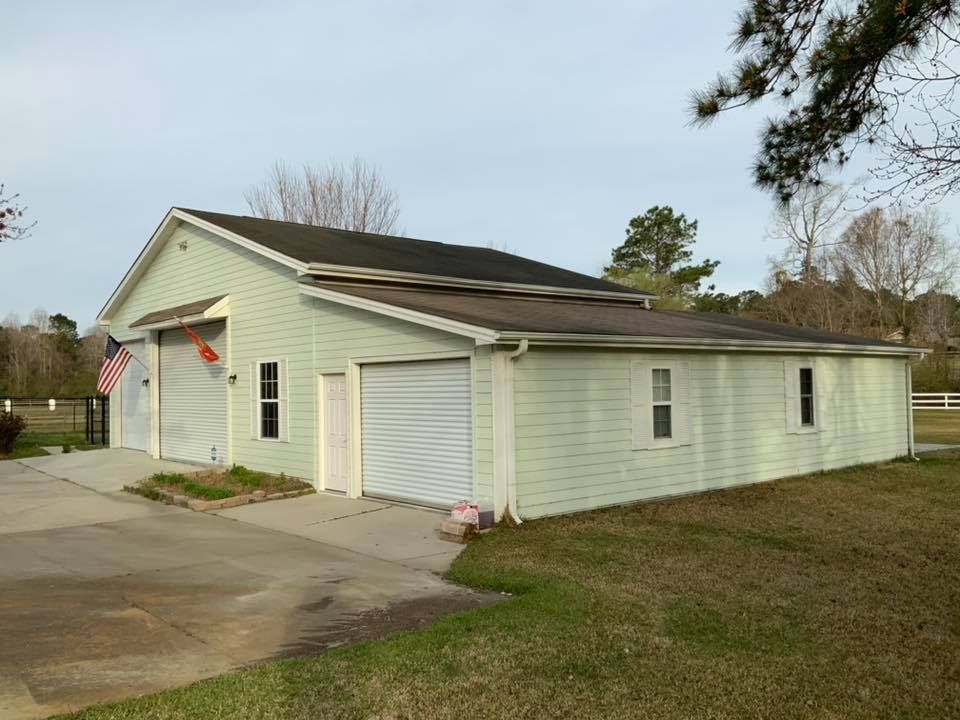 Light-colored detached garage with two roll-up doors beside a driveway and grassy yard