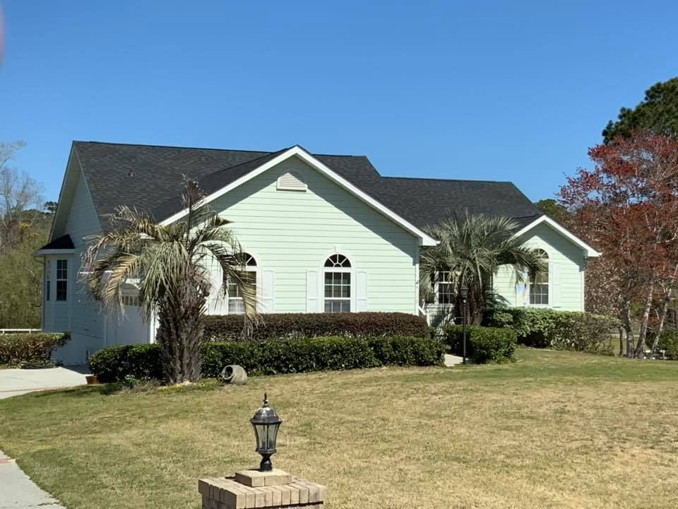 Suburban house with pale green siding, dark roof, and a manicured lawn under a clear blue sky