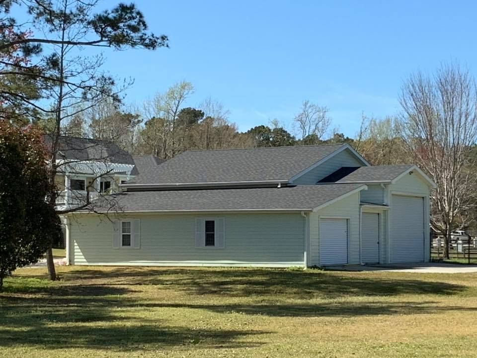 White single-story house with gray roof and two garage doors beside a grassy yard under a clear blue sky