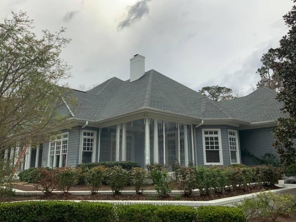 Gray single-story house with white trim, a hip roof, and manicured shrubs under an overcast sky