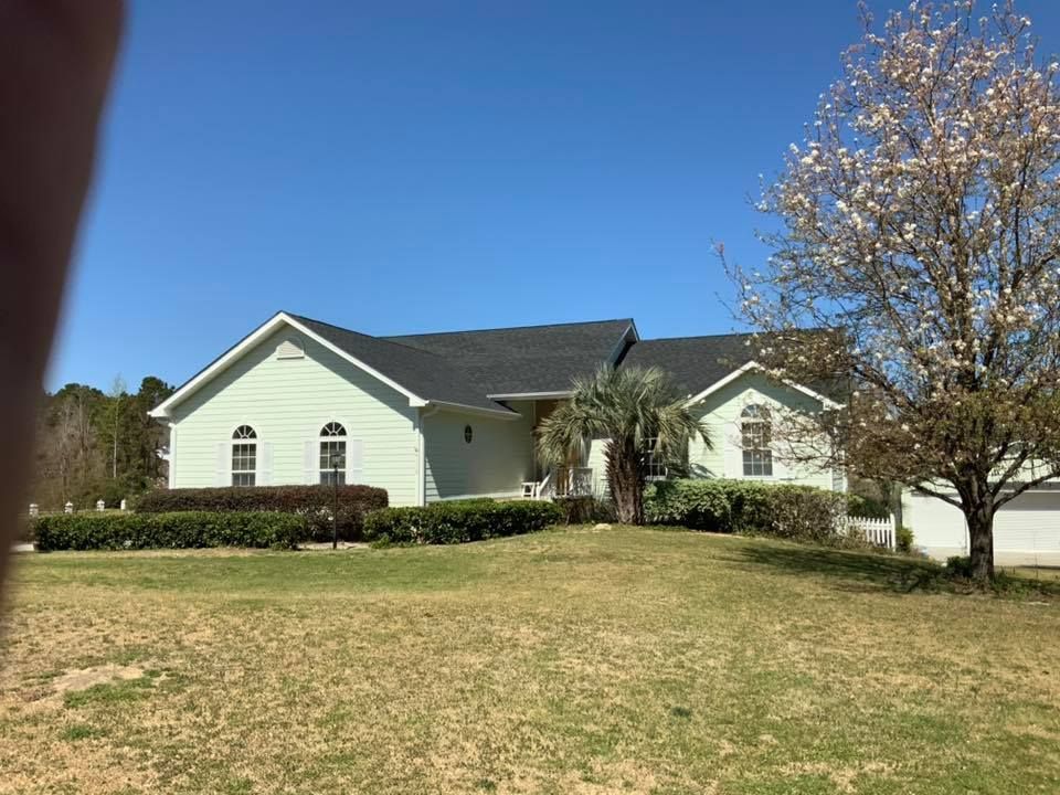Single-story white house with dark roof and arched windows on a grassy lawn under a blue sky