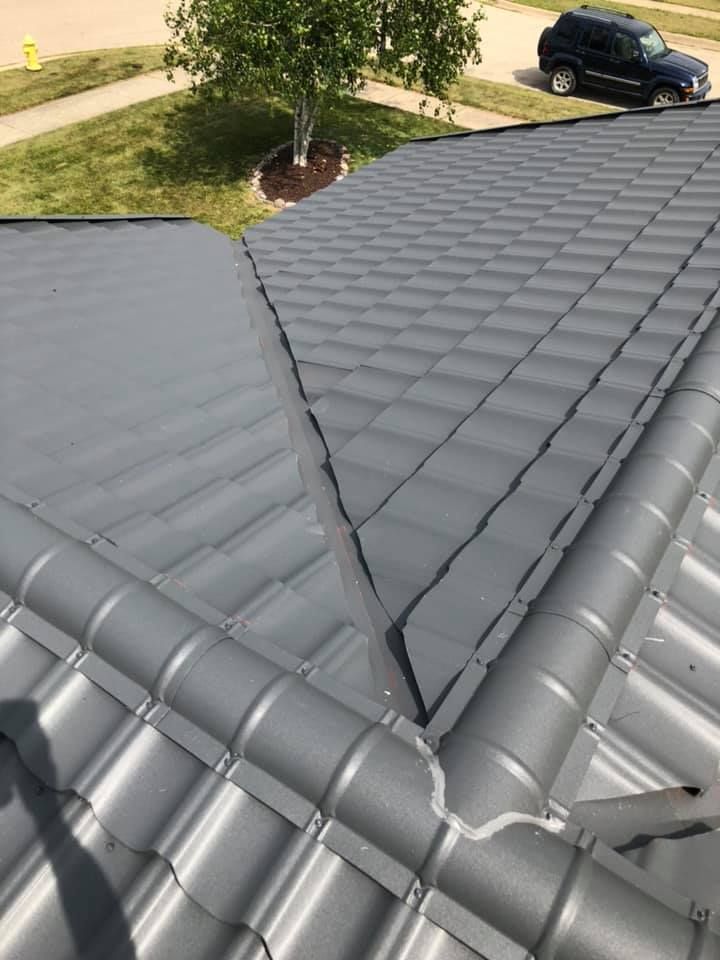 Gray metal roof with intersecting ridges, seen from above near a driveway and parked SUV