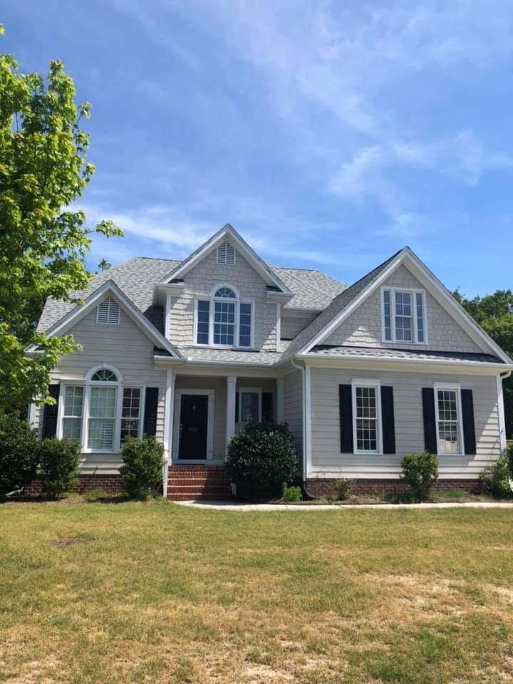 Suburban gray house with white trim, front porch, and a dry lawn under a blue sky