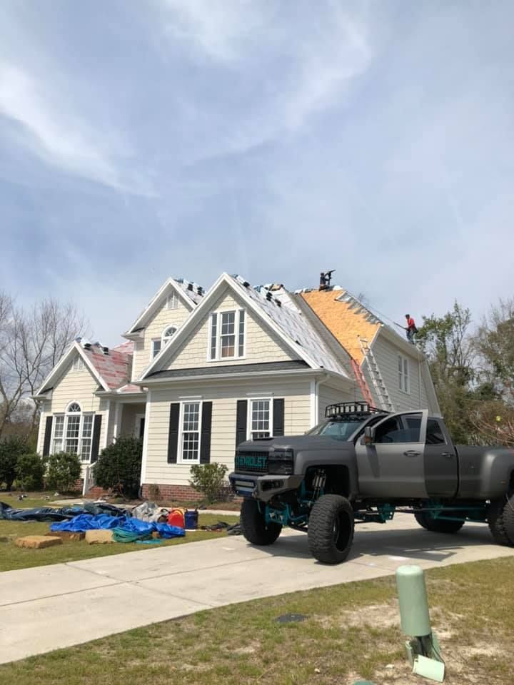 House under roof repair with workers, black pickup truck, and roofing materials in driveway