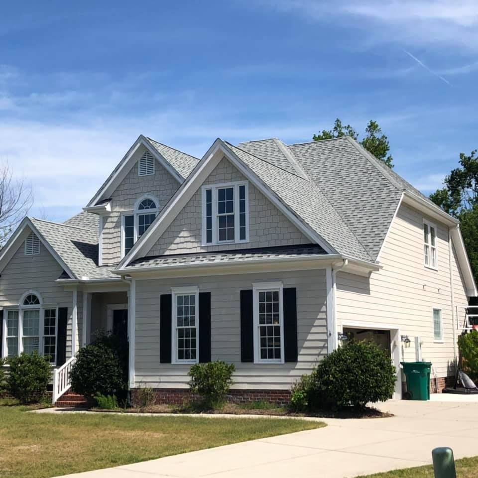 Suburban house with gray siding, white trim, and a peaked roof under a blue sky