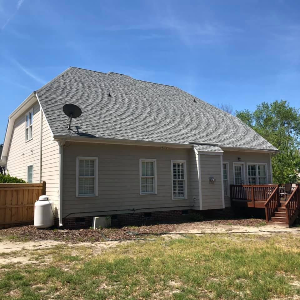 Beige house with gray roof, satellite dish, wooden deck, and small yard under a blue sky