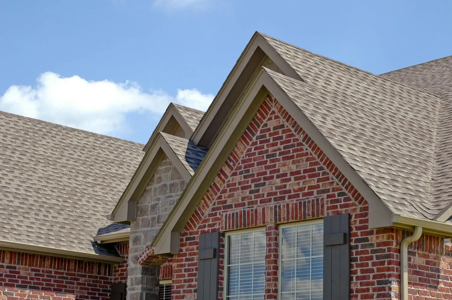 Brick house roof and gables against a blue sky with clouds