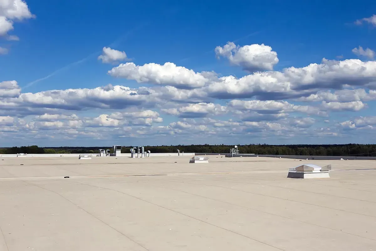Wide beige rooftop under a blue sky with scattered clouds and distant equipment