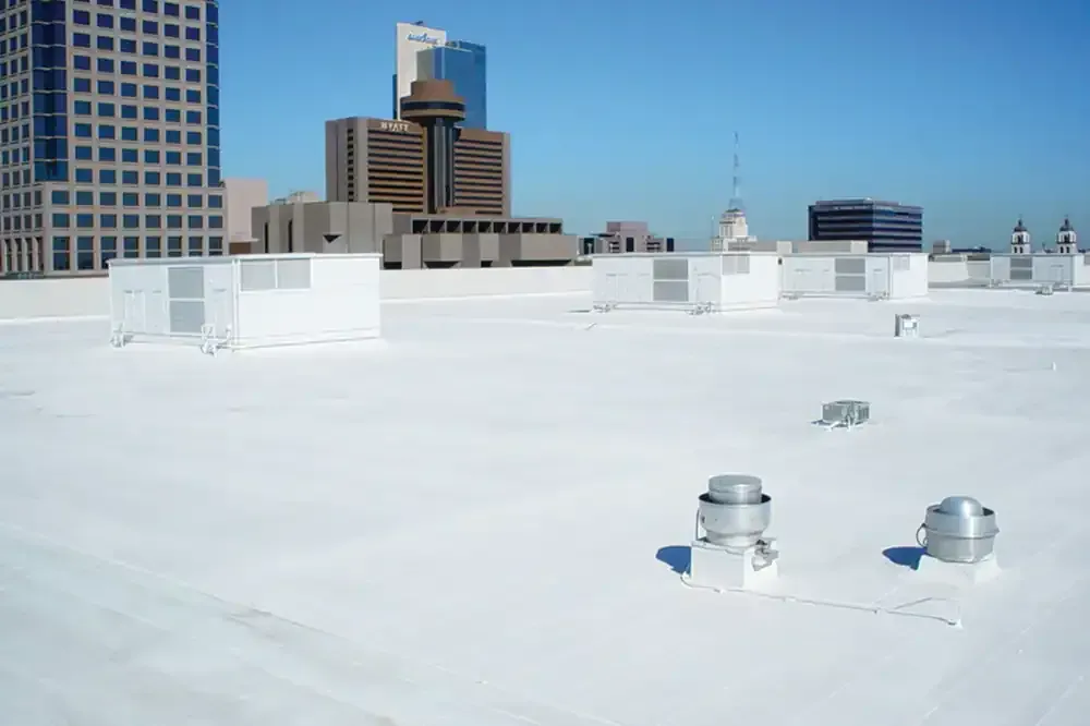 Rooftop with white coating, vents, and city buildings under a clear blue sky