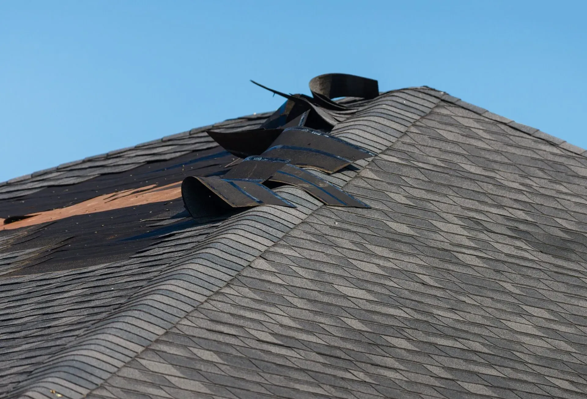 Roof with damaged shingles and exposed black vents under a clear sky