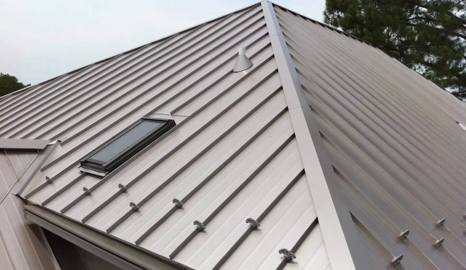Close-up of a gray metal roof with skylights and safety anchors under cloudy skies