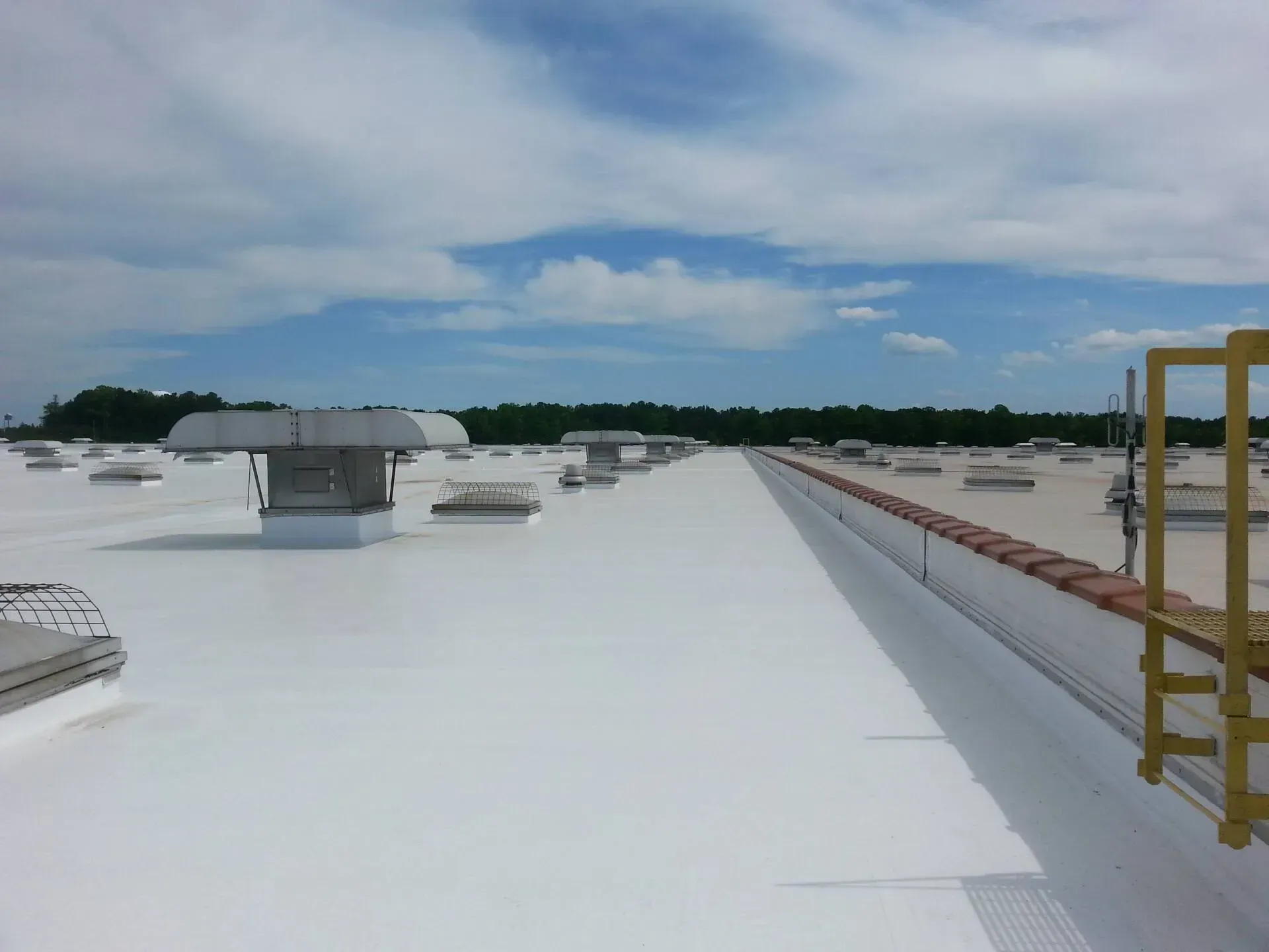 Flat white rooftop with ventilation units under a cloudy blue sky, yellow ladder at right