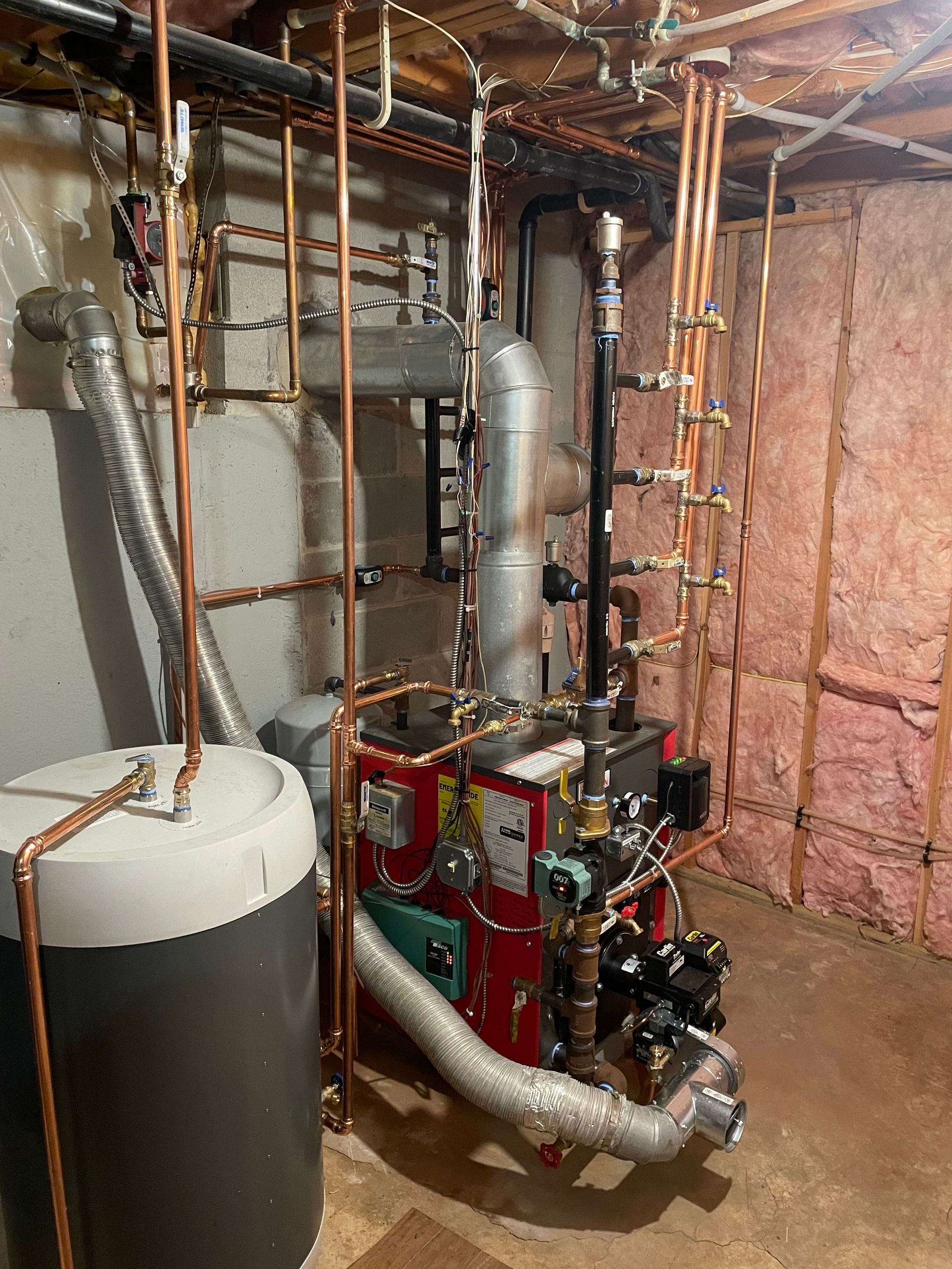A boiler is sitting in a basement next to a water heater.