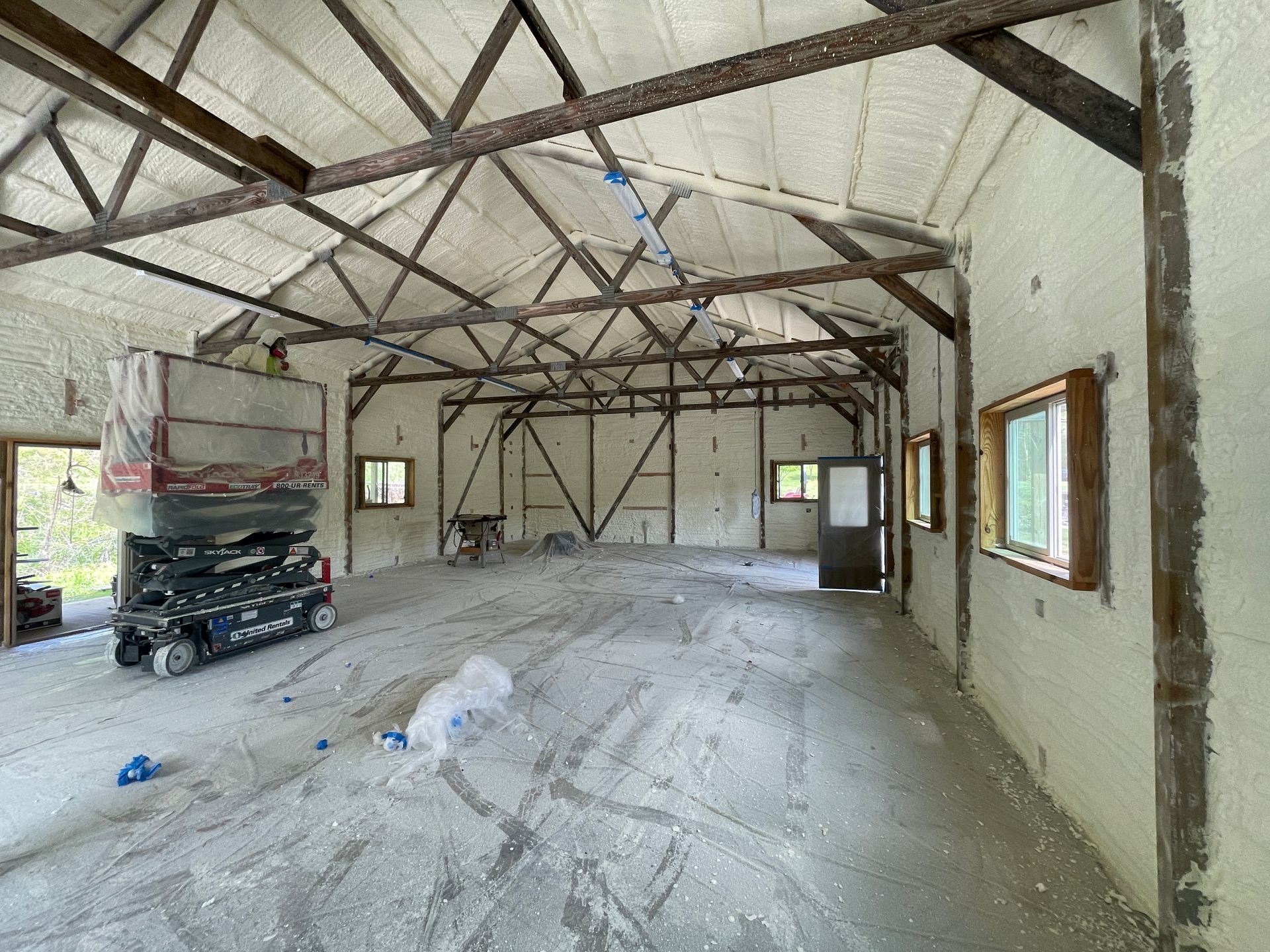 Interior view of a barn under construction with exposed wooden beams, spray foam insulation, and a scissor lift.