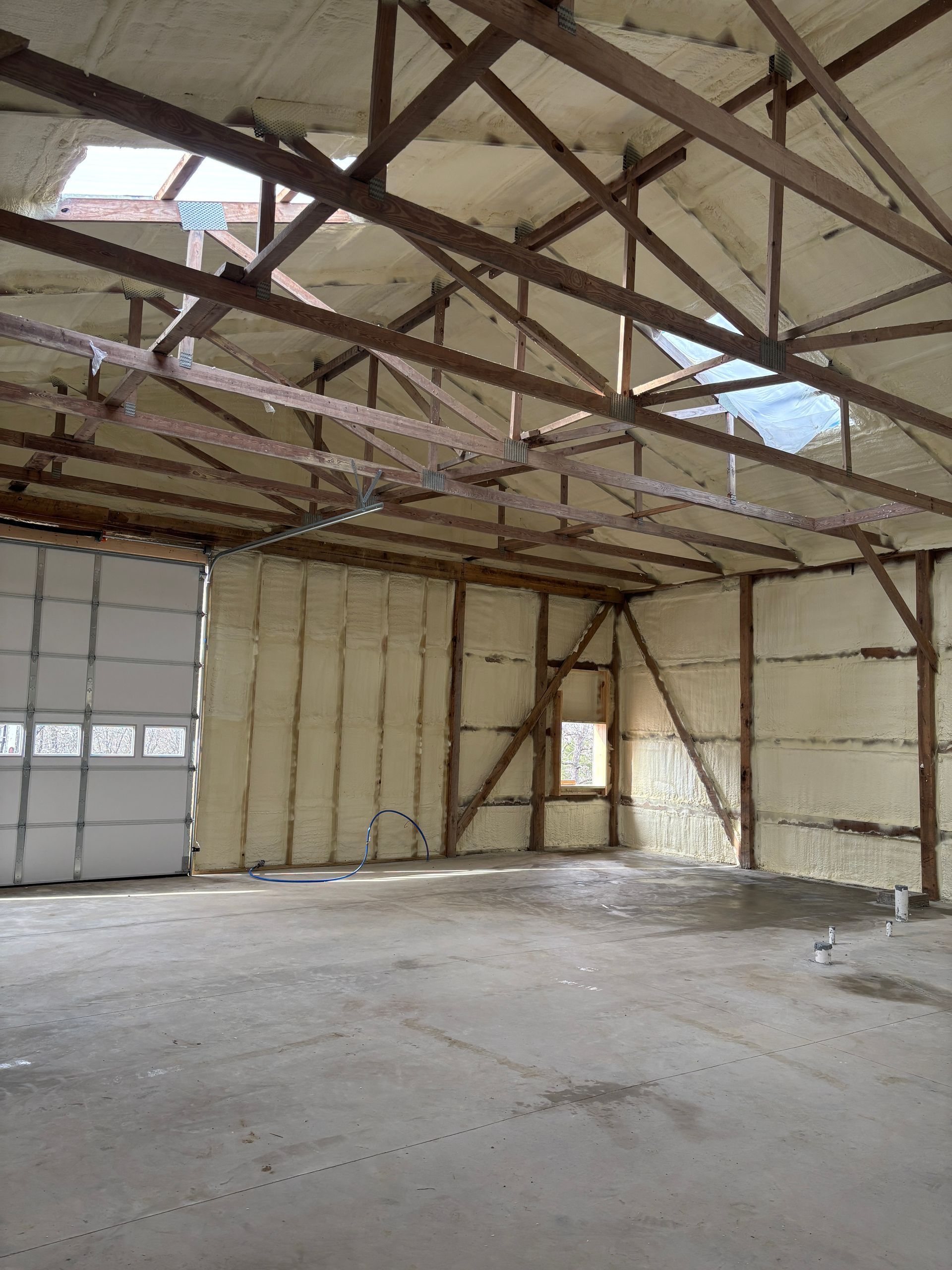 Interior of a large building with exposed wooden beams, foam insulation, and a concrete floor.