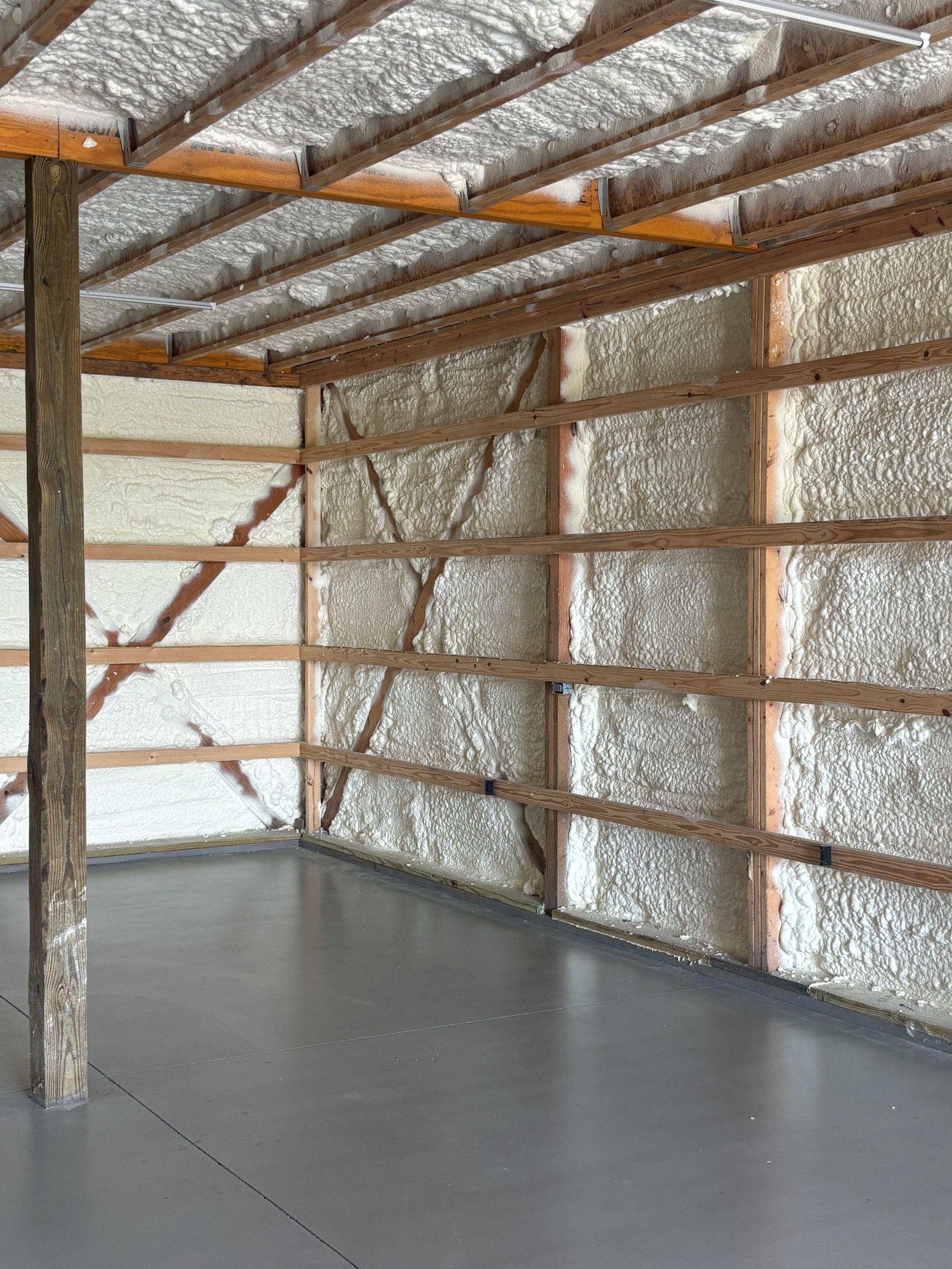 Interior of a barn with light gray concrete floor and walls and ceiling insulated with white foam. Wooden frame visible.