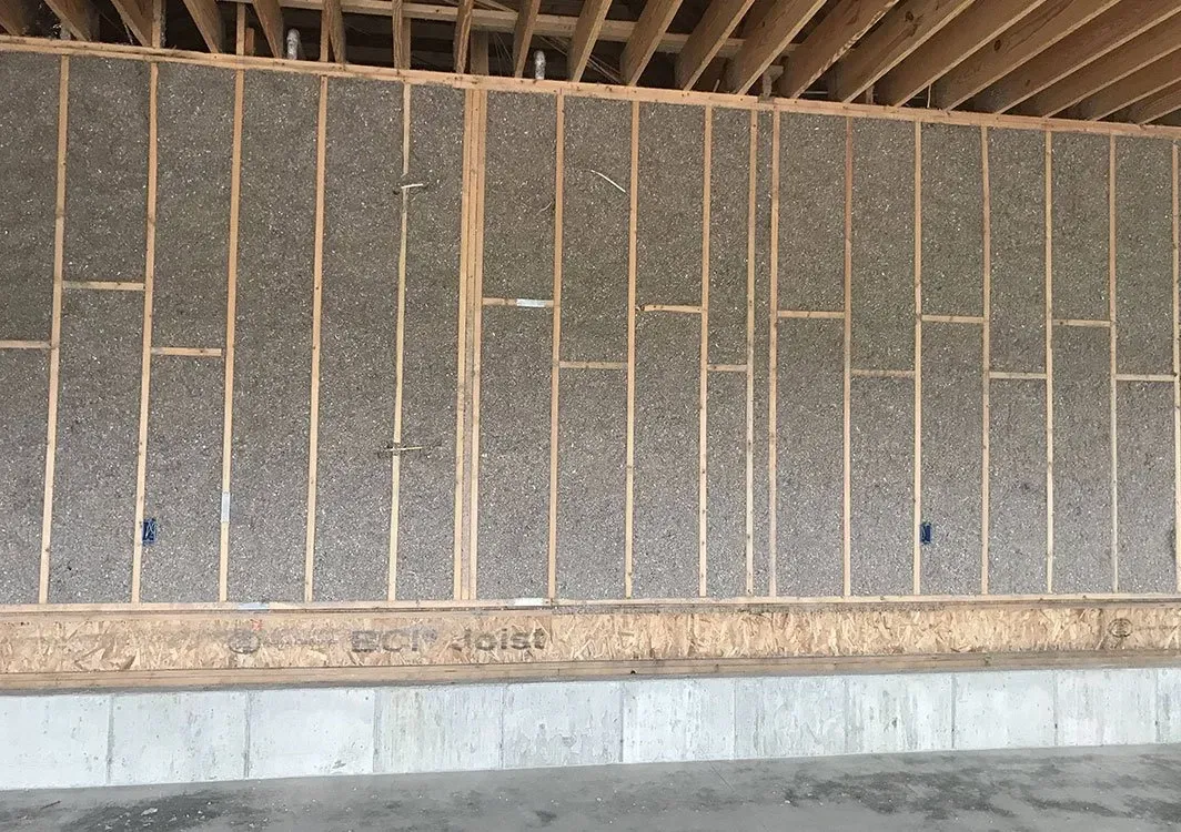 Wall under construction with exposed wooden framing and insulation between studs.