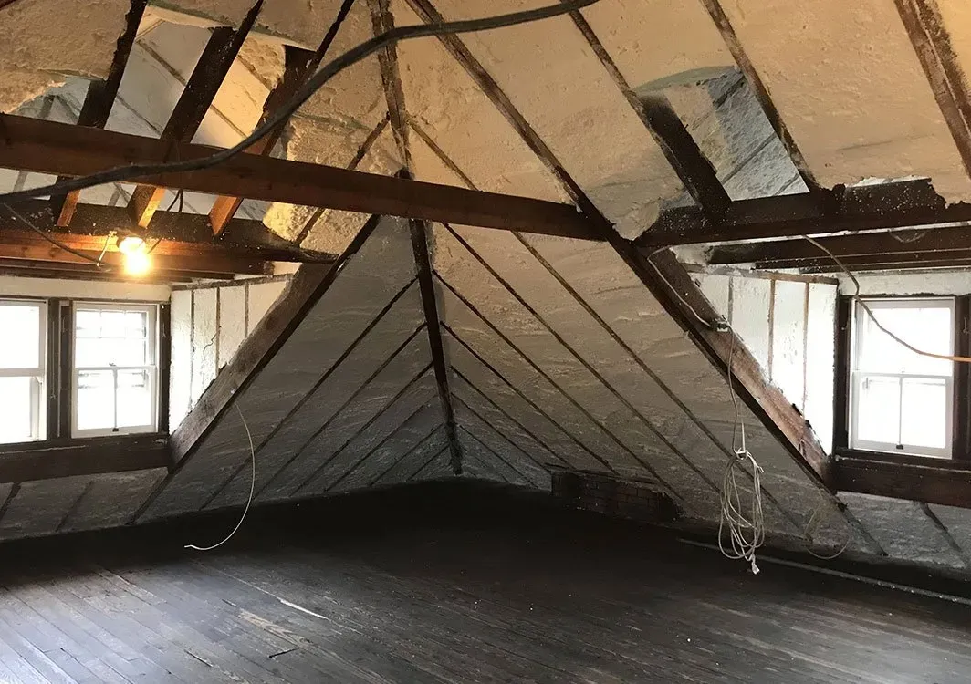 Attic interior with exposed beams, angled walls, two windows, and dark wood floor.