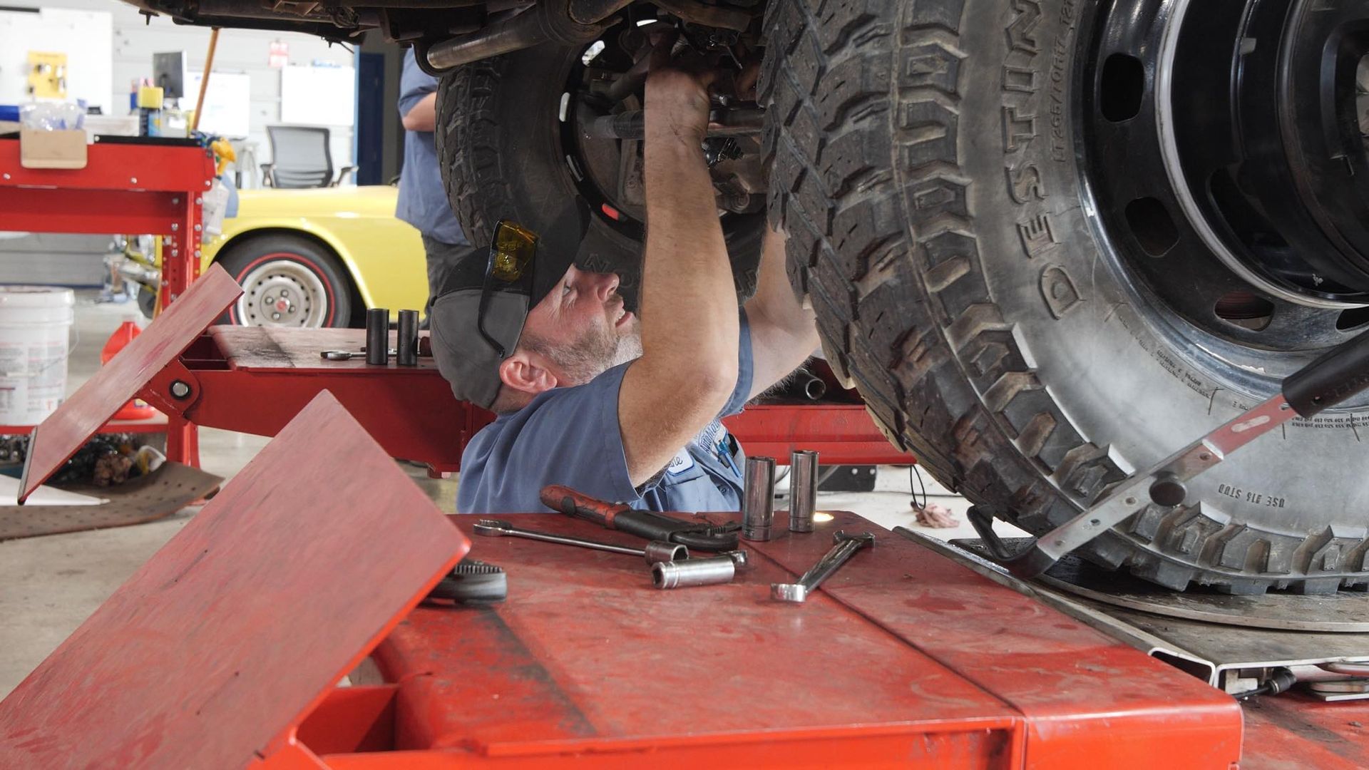 A man is working on a tire on a lift in a garage.