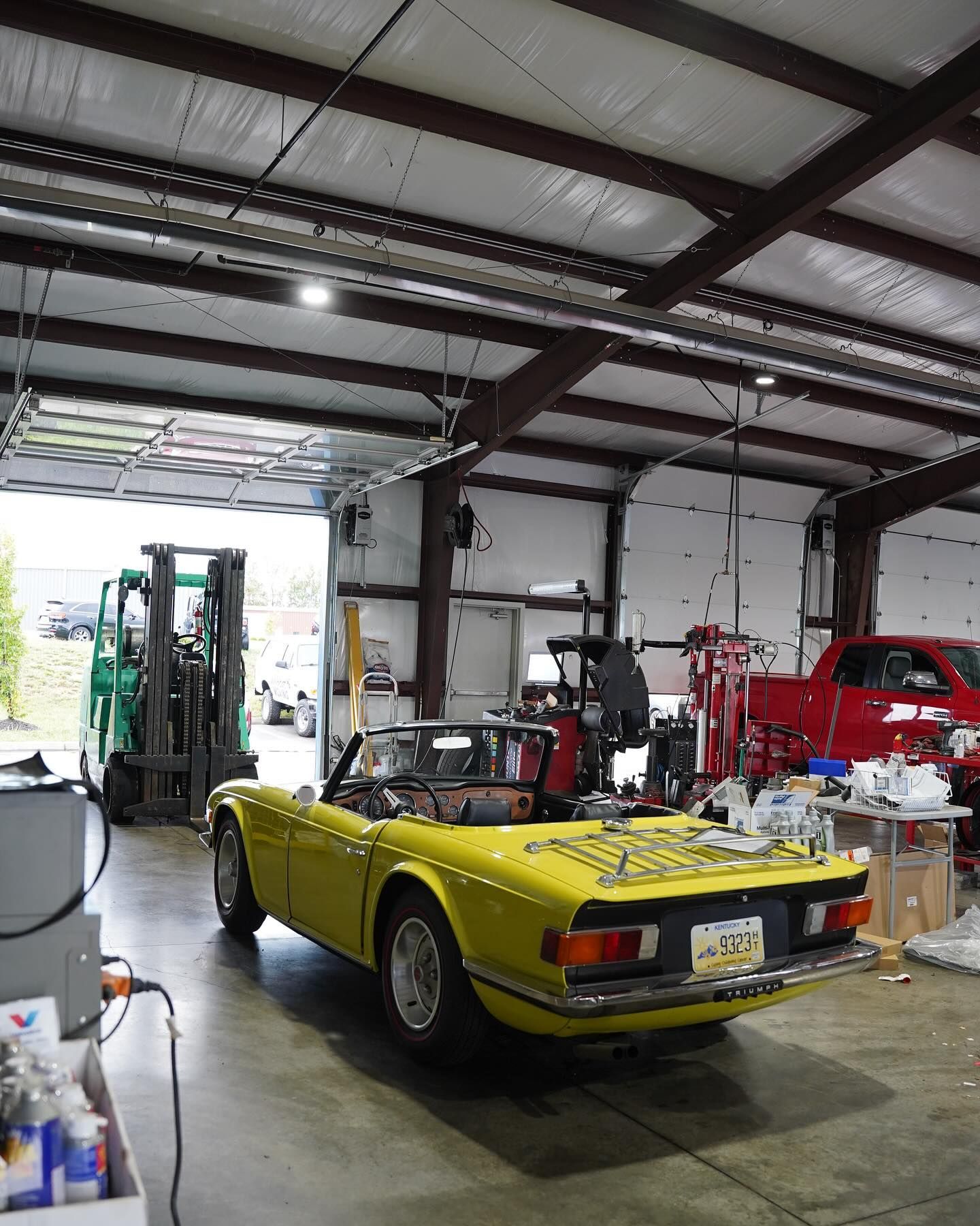 A yellow car is parked in a garage with a forklift in the background