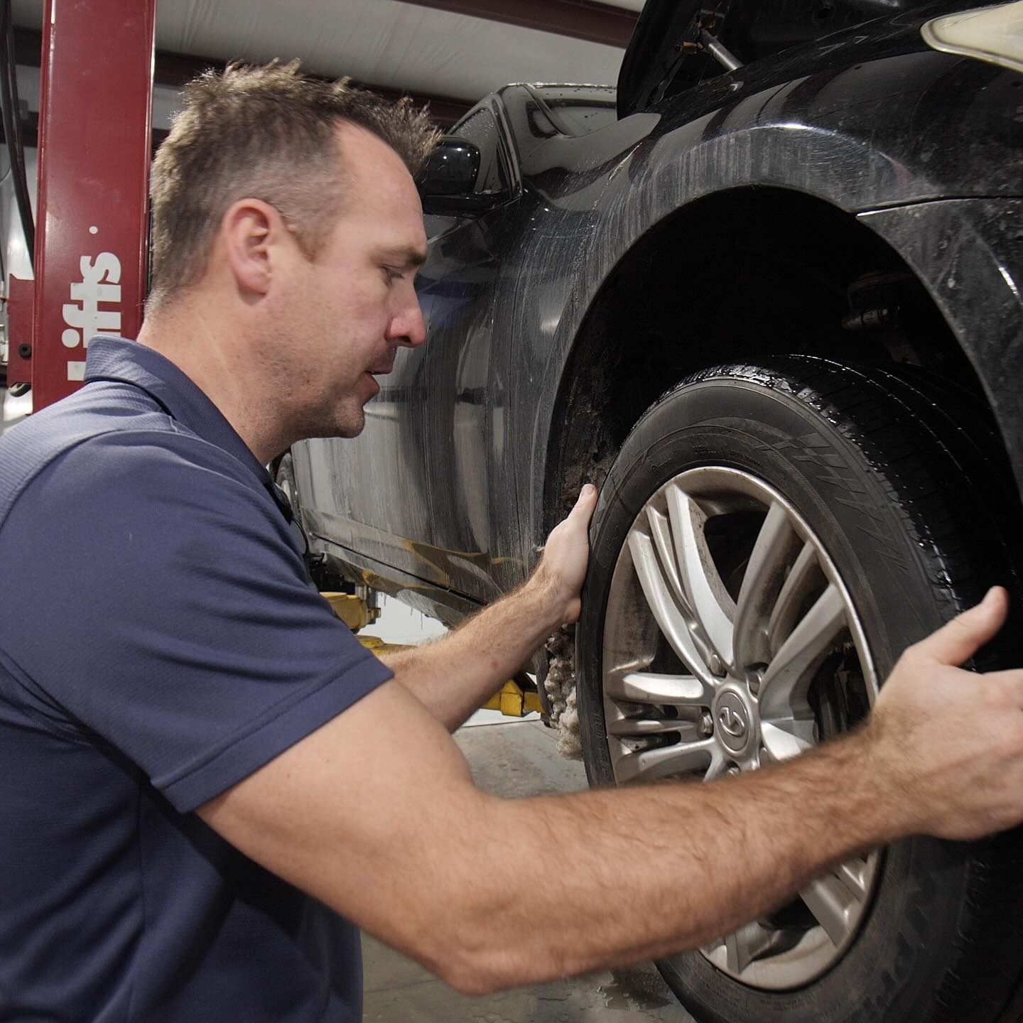 A man in a blue shirt is working on a car wheel