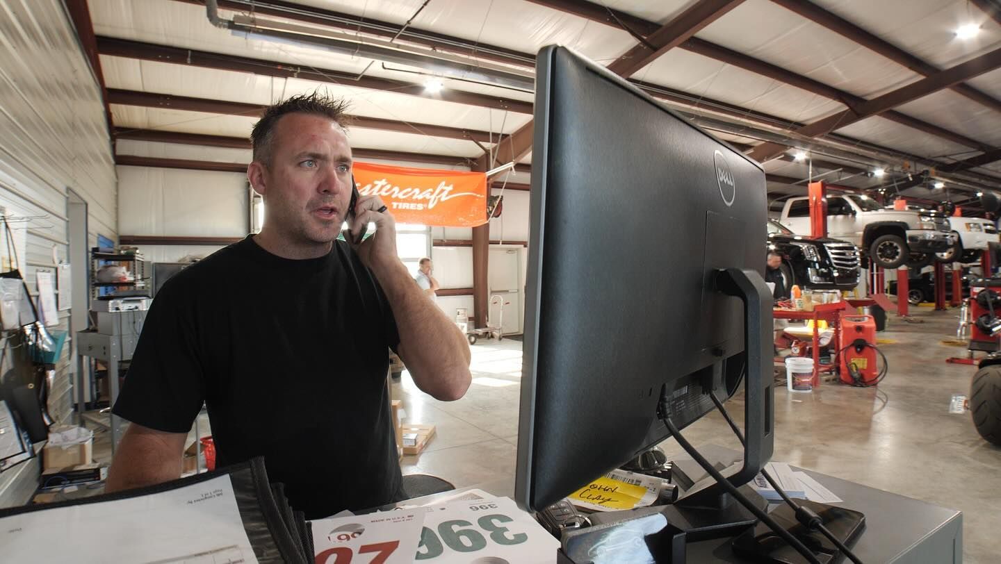 A man is talking on a cell phone in front of a computer in a garage.